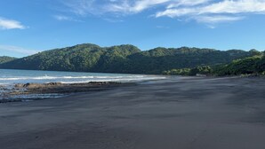 Una playa con costa rocosa y una colina boscosa al fondo.