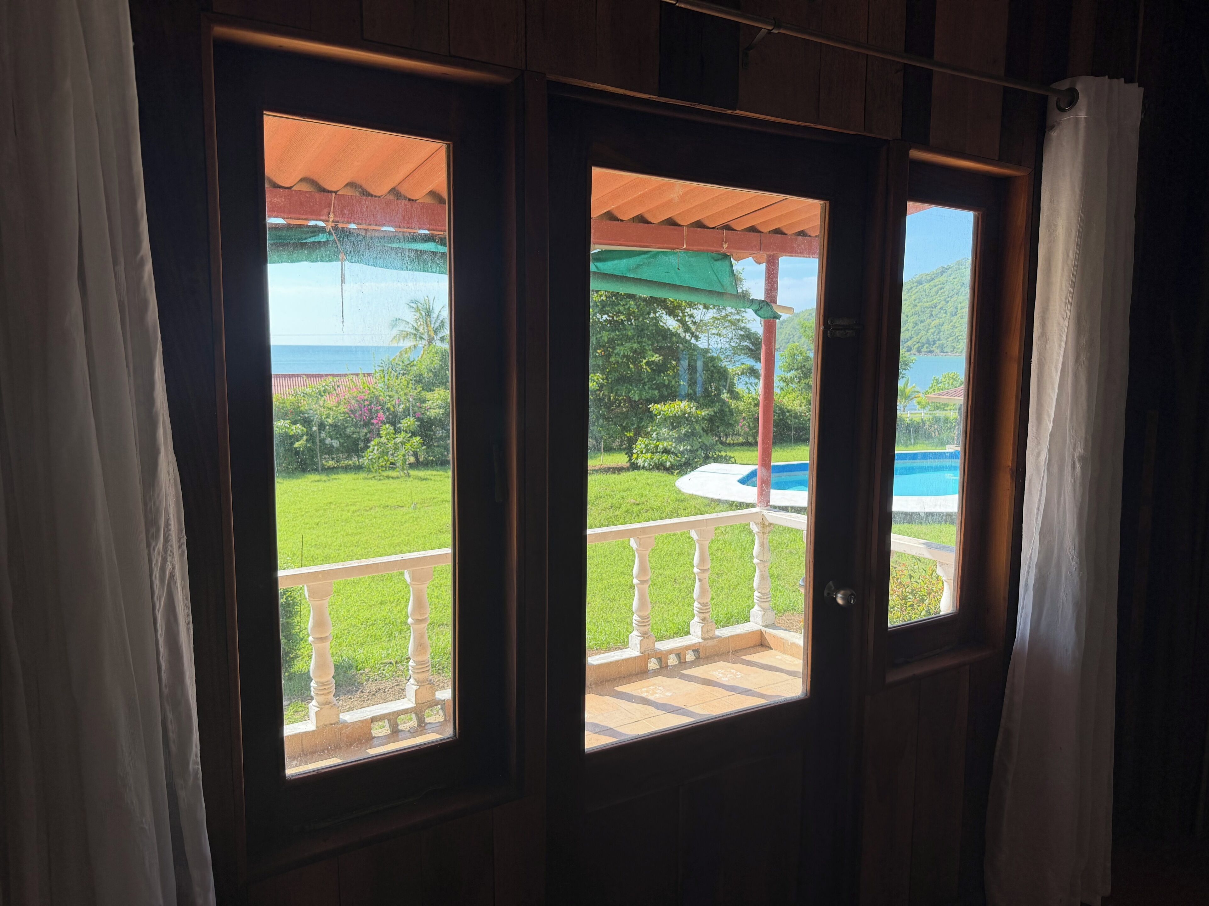 Blick von einem Zimmer mit einer Holztür, die zu einem Außenbereich mit Pool und Grünflächen führt.