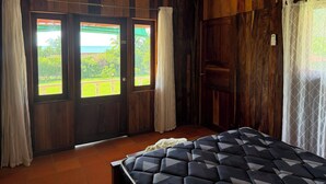 Una habitación con paneles de madera, una cama con cubrecolcha estampado y vistas a un balcón a través de una puerta.