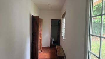 Un pasillo estrecho con un banco de madera, una puerta que da a un baño y una ventana con vistas a zonas verdes.