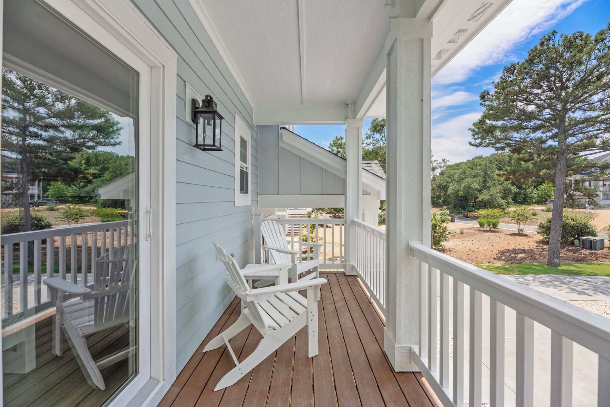 A covered porch with white railings, a wooden deck, and two Adirondack chairs.