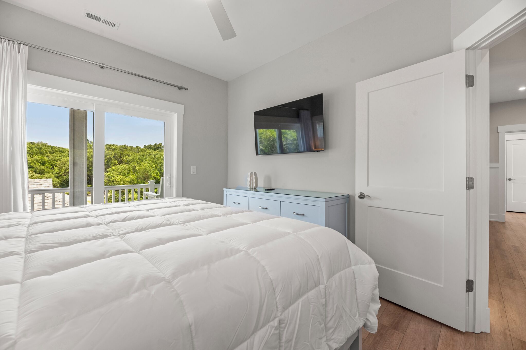 Une chambre dotée d’un grand lit, d’une commode, d’un téléviseur fixé au mur et d’une porte-fenêtre coulissante donnant sur un balcon.