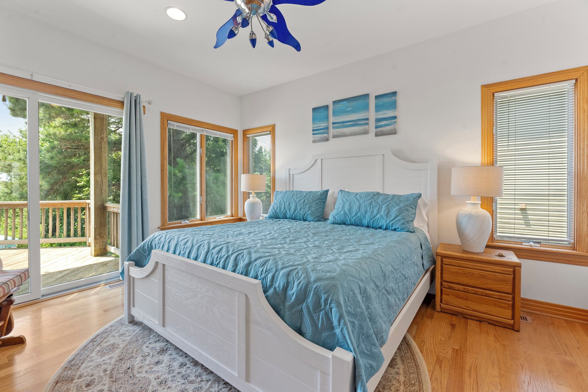 A bedroom with a large bed, two bedside tables, a ceiling fan, and a view of the outdoors.