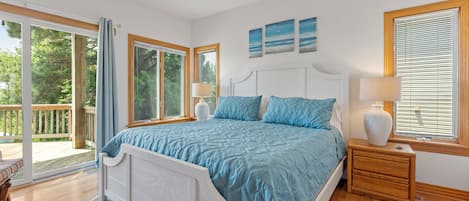 A bedroom with a large bed, two bedside tables, a ceiling fan, and a view of the outdoors.
