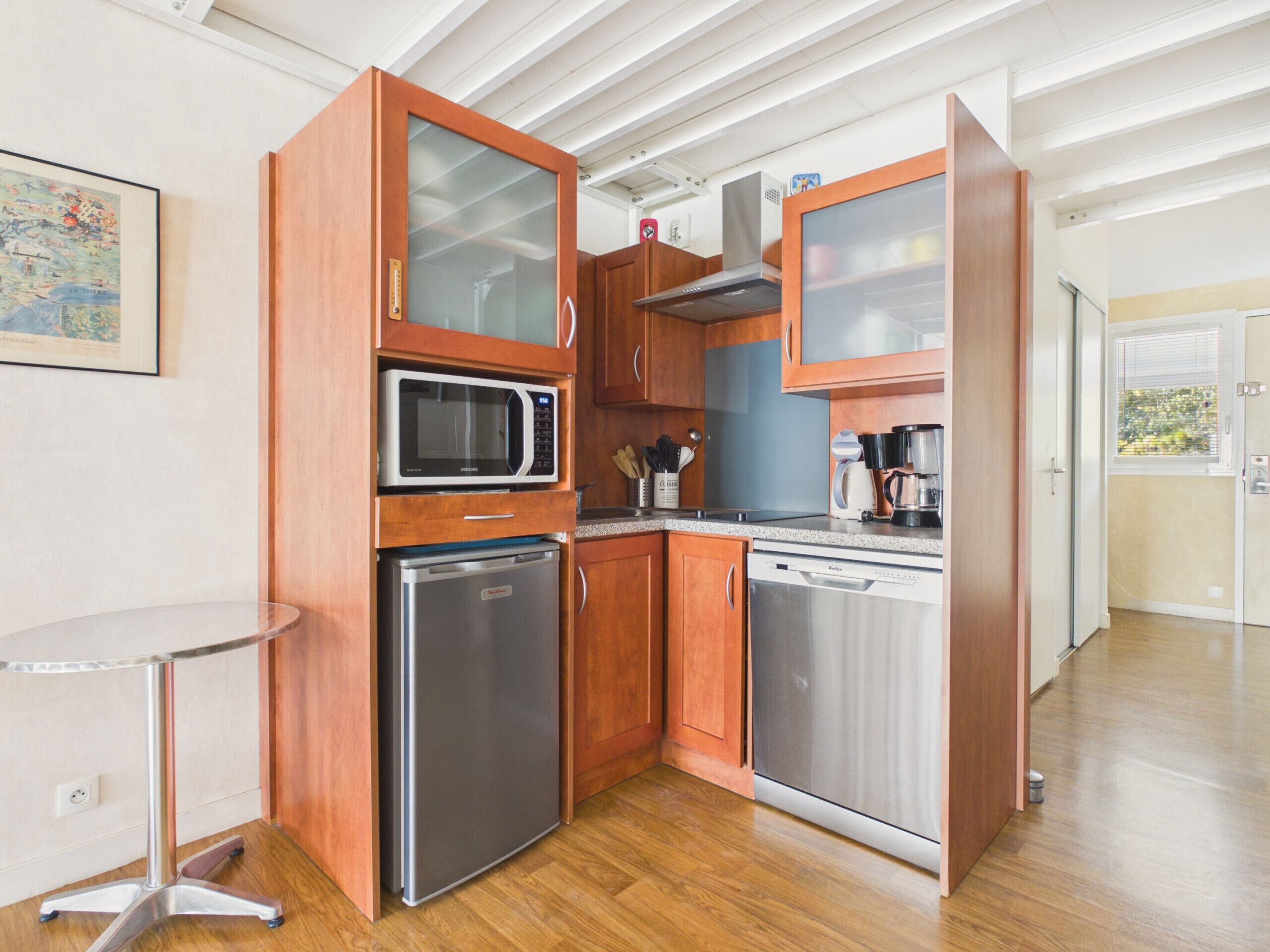 Una cocina compacta con electrodomésticos integrados, una pequeña mesa redonda y armarios de madera.