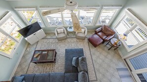 A sunroom with a ceiling fan, two sofas, a coffee table, and a TV. - Mr and Mrs Sea: Beach Club Access w/ Pool | Golf Course Views (Nags Head)