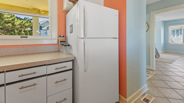 A kitchen with a white refrigerator, a window, and a door leading to another room. - Mr and Mrs Sea: Beach Club Access w/ Pool | Golf Course Views (Nags Head)