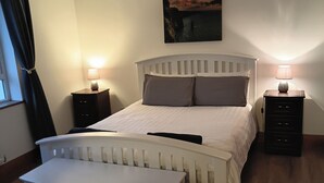 Een slaapkamer met een bed, nachtkastjes, een stoel en een schilderij aan de muur.