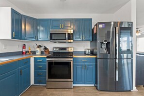 A kitchen with blue cabinets, stainless steel appliances, a microwave, oven, and a refrigerator. - Canalfront | Private Boat Dock | Hot Tub | Pool Access (Nags Head)