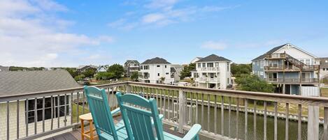 A deck with two chairs and a table overlooking a body of water with buildings in the background.