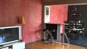 A room with a wooden floor, a flat-screen TV, a dining table with chairs, and a red accent wall. - Vacation Rental in the Somme Bay Area for 6 People (Fort-Mahon-Plage)