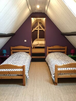 Ein kleines, dreieckiges Schlafzimmer im Dachgeschoss mit zwei Holzbetten, einem Bett in der Mitte und einer geneigten Decke.