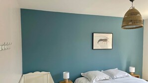 A bedroom with a teal wall, a bed with white bedding, two bedside tables with lamps, and a hanging light fixture. - The Spot in the Baie de Somme (Quend)