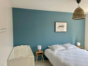 Ein Schlafzimmer mit einer Türkis wand, einem Bett mit weißer Bettwäsche, zwei Nachttischen mit Lampen und einer Hängelampe.