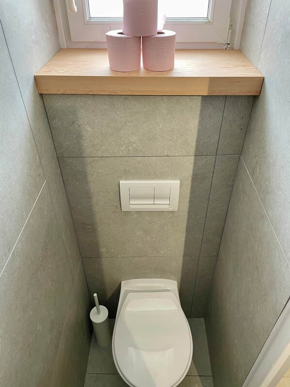 Et lille badeværelse med toilet, bidét og et vindue over toilettet.