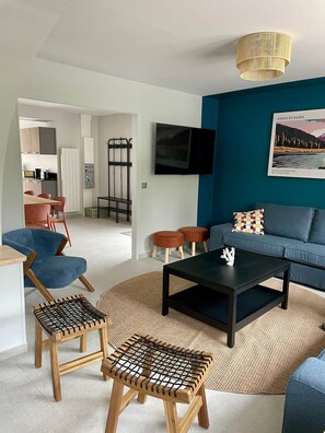 Ein modernes Wohnzimmer mit blauer Akzentwand, einem Flachbildfernseher, einem Couchtisch und Sitzgelegenheiten, darunter eine Couch und Sessel.