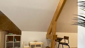 A room with a sloped ceiling, a wooden bookshelf, a small wooden table, a chair, and a wooden beam structure. - La Menuiserie in the Baie de Somme: 15 people (Fort-Mahon-Plage)