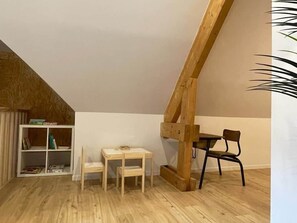Ein Zimmer mit schrägem Dach, einem Holzbücherregal, einem kleinen Holztisch, einem Stuhl und einer Holzträgerkonstruktion.