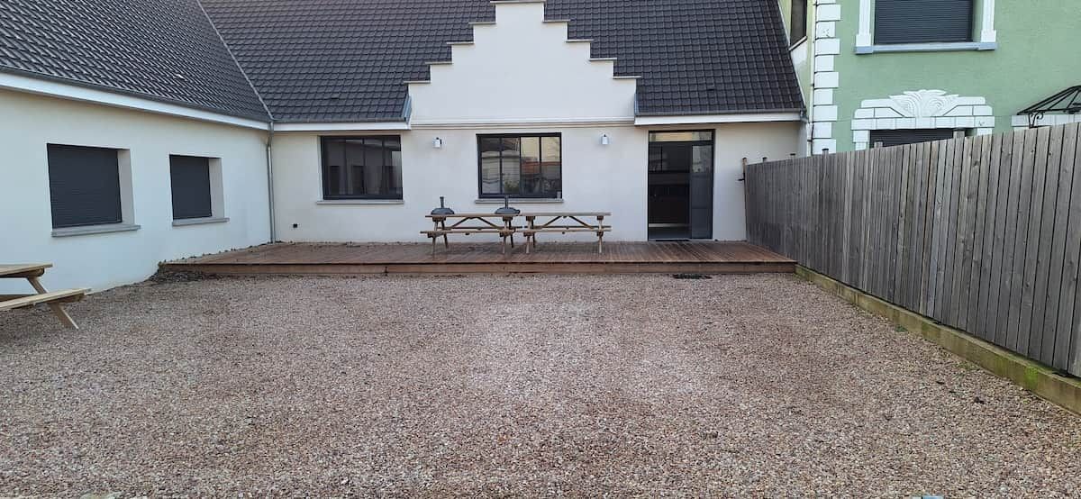 Une terrasse en gravier avec un banc en bois et une table, le tout entouré d’une clôture en bois.