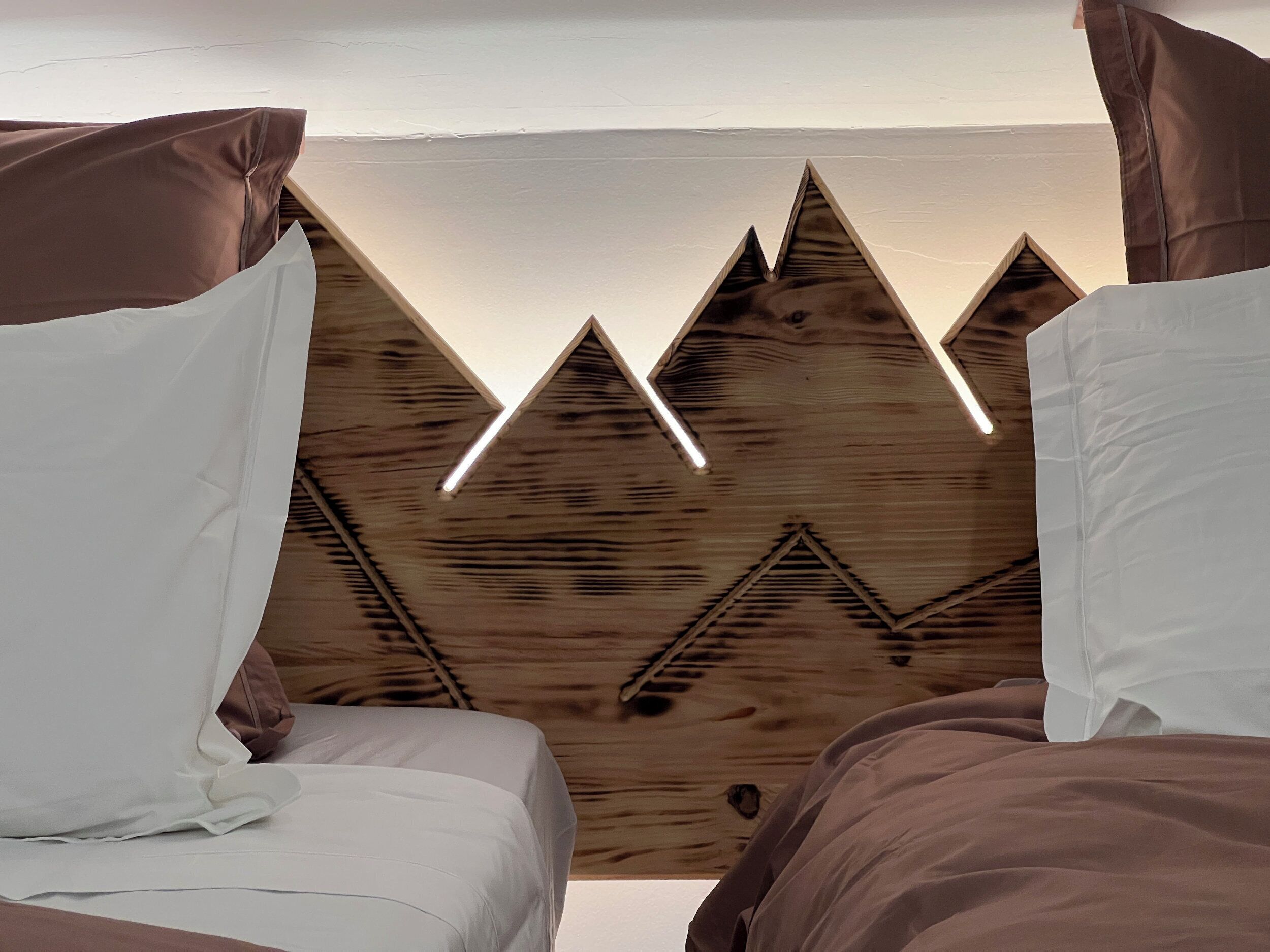Una habitación con dos camas, una pared de madera con motivos de montaña y una lámpara en el techo.