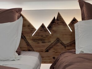 Une chambre avec deux lits, un mur en bois orné d’un motif de montagne et un luminaire au plafond.