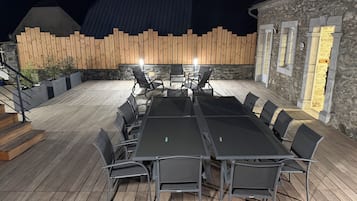 Een buitenterras met een lange tafel en stoelen, omgeven door stenen muren en houten omheining.