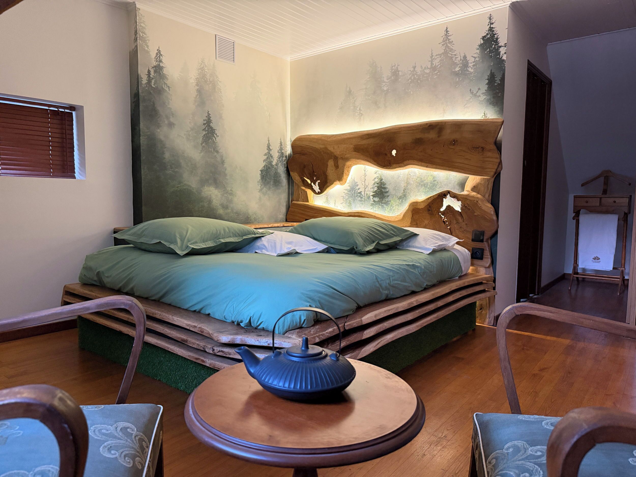 Une chambre à coucher avec un lit, une table ronde sur laquelle se trouve une théière, et une commode.