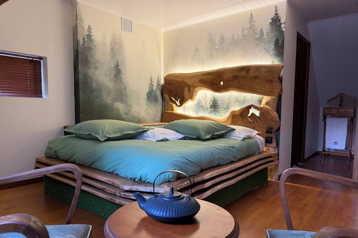 Une chambre à coucher avec un lit, une table ronde sur laquelle se trouve une théière, et une commode.