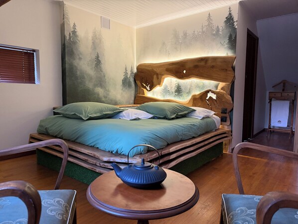 Une chambre à coucher avec un lit, une table ronde sur laquelle se trouve une théière, et une commode.