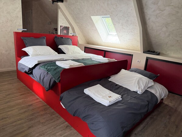 Un dormitorio con estructura de cama roja, dos camas, un tragaluz y suelo de madera.