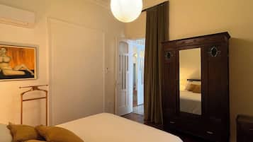 Un dormitorio con cama, espejo, armario y un cuadro en la pared.