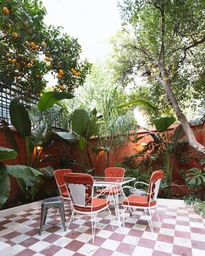A patio with a checkered floor, surrounded by lush greenery and orange fruit trees. - Entire Athens Townhouse | Private Garden (Athina)