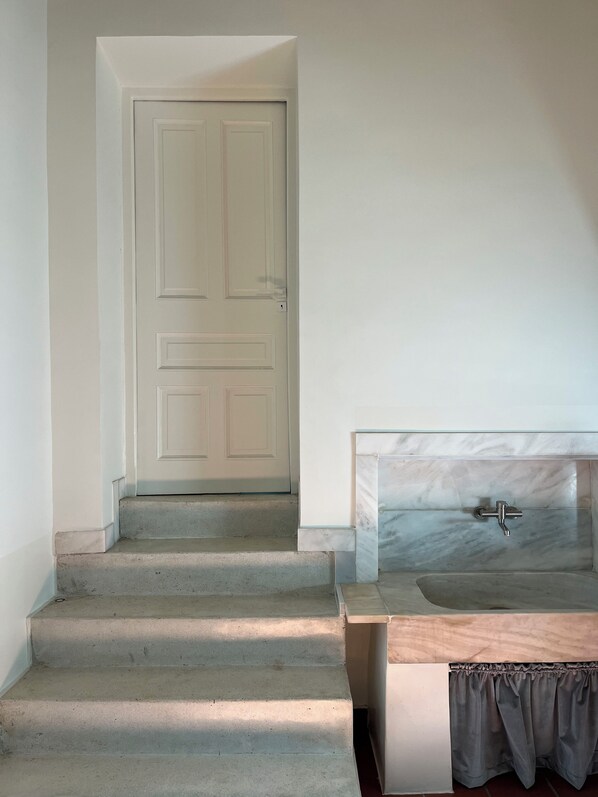 Une salle de bain avec un lavabo en marbre, un espace douche et une porte donnant sur une autre pièce.
