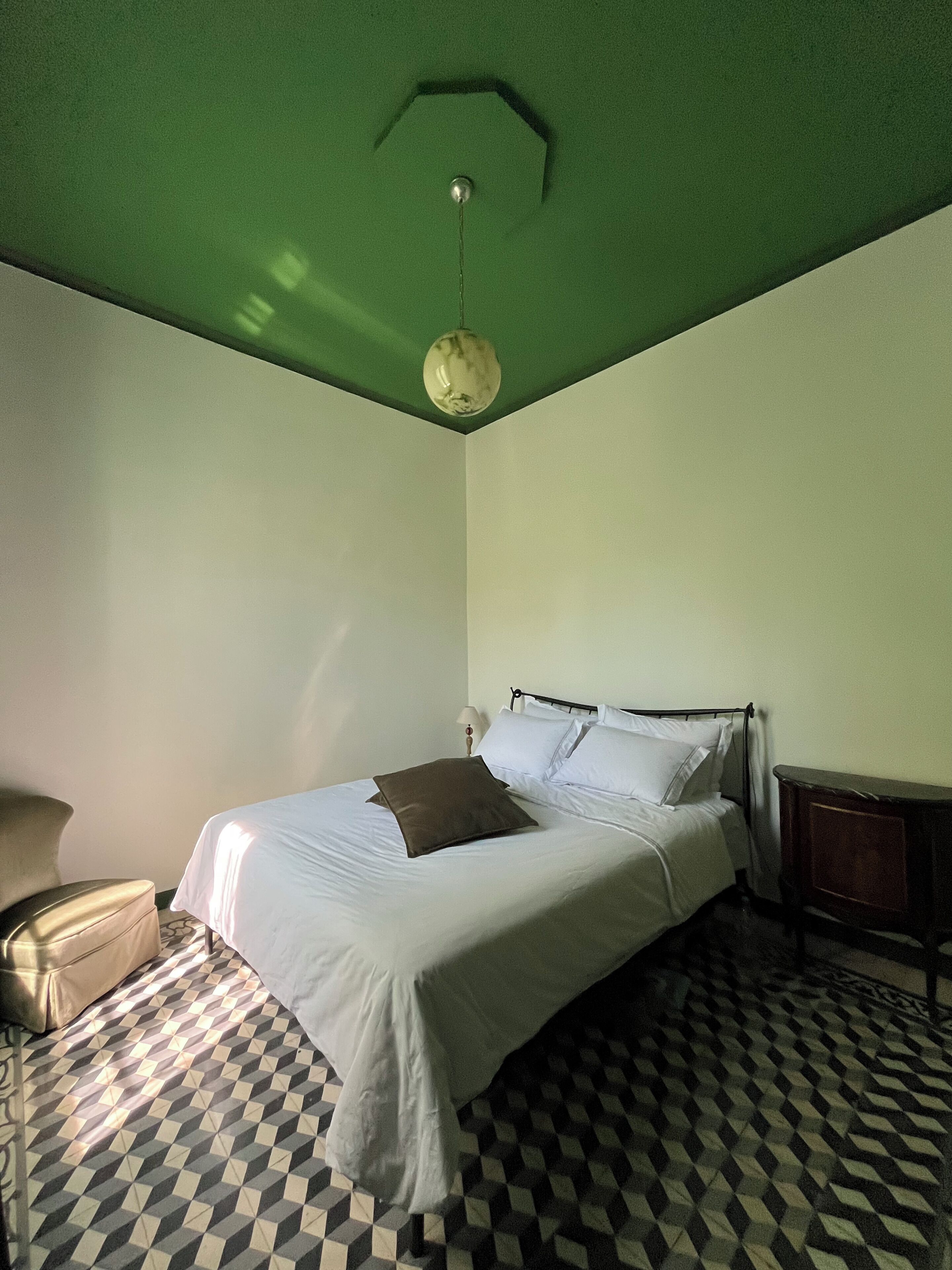 A room with a bed, a chair, a lamp, and a patterned floor.