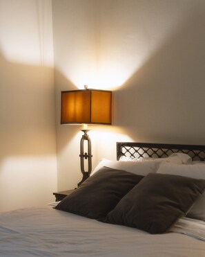 A bed with a headboard, a bedside lamp, and a wall with a light source casting shadows. - Entire Athens Townhouse | Private Garden (Athina)