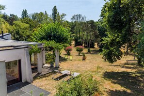 Ein Wohnhaus mit Terrasse, einer Pergola und einem Garten mit unterschiedlichen Pflanzen und einer Bank.