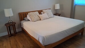 A bedroom with a wooden bed, two bedside tables with lamps, and a window with blinds. - Cozy 3-bedroom home with heated pool and spa in relaxing Cape Coral. (Cape Coral)