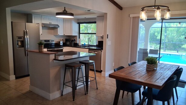 A modern kitchen with a central island, bar stools, and a dining table with chairs. - Cozy 3-bedroom home with heated pool and spa in relaxing Cape Coral. (Cape Coral)