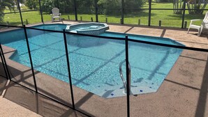 A swimming pool with a safety fence, a hot tub, and a covered patio area with chairs. - Cozy 3-bedroom home with heated pool and spa in relaxing Cape Coral. (Cape Coral)