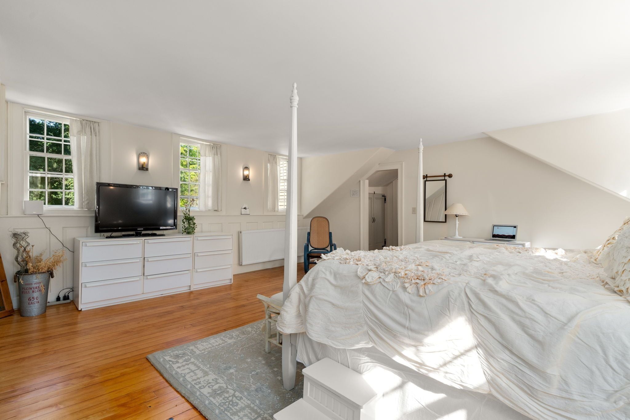Un dormitorio con cama con dosel, televisor, cómoda y una silla.