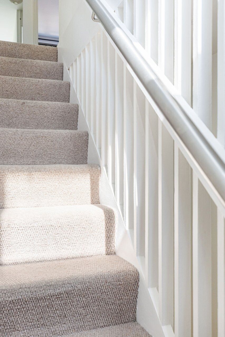 Una escalera con barandilla blanca y peldaños cubiertos de moqueta color beige.