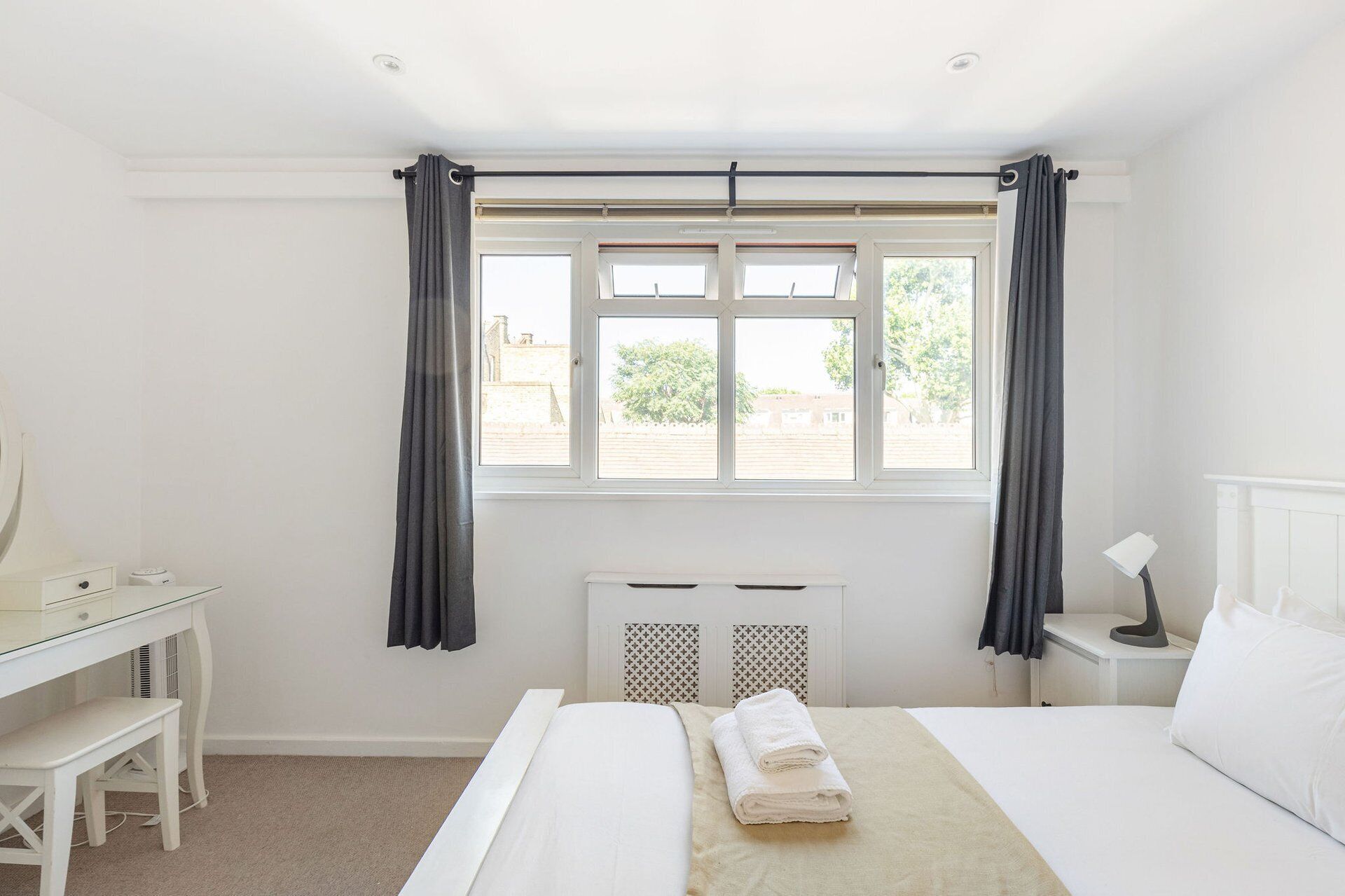 A hotel room with a bed, a desk, a chair, a radiator, and a window with curtains.