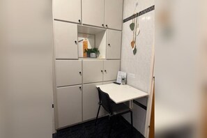 Ein kleiner Raum mit einem weißen Schreibtisch, einem schwarzen Stuhl und einem weißen Schrank mit vielen Fächern.