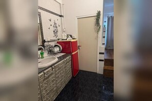 Eine kleine Küche mit Spüle, einem roten Kühlschrank und einer Tür mit einer Pflanze.