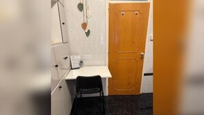 Um quarto pequeno com uma escrivaninha, uma cadeira, uma porta de madeira e piso de azulejos.