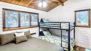 A bunk bed room with a ceiling fan, wooden walls, and windows with blinds.