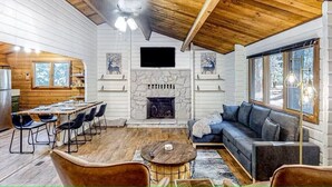 A cozy cabin interior with a stone fireplace, a dining area, and a seating area with a sofa and chairs.