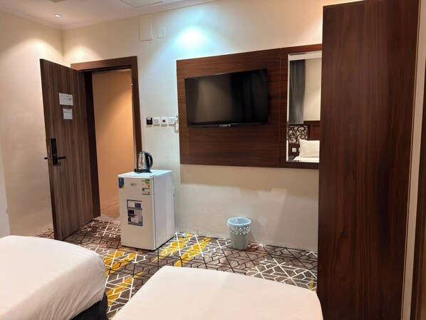 A hotel room with two beds, a television, a minibar, and a patterned floor. - Manask Al Bayt Hotel (Makkah)