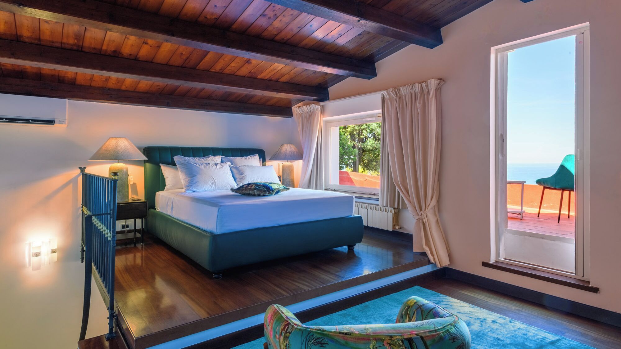 Une chambre à coucher comprenant un lit, une table de chevet, une lampe, une fenêtre avec des rideaux et une vue sur l’extérieur.