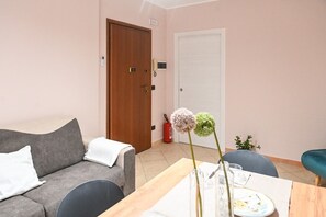 Ett rum med en grå soffa, en trädörr, en vit dörr och ett litet bord med en vas och en tallrik.